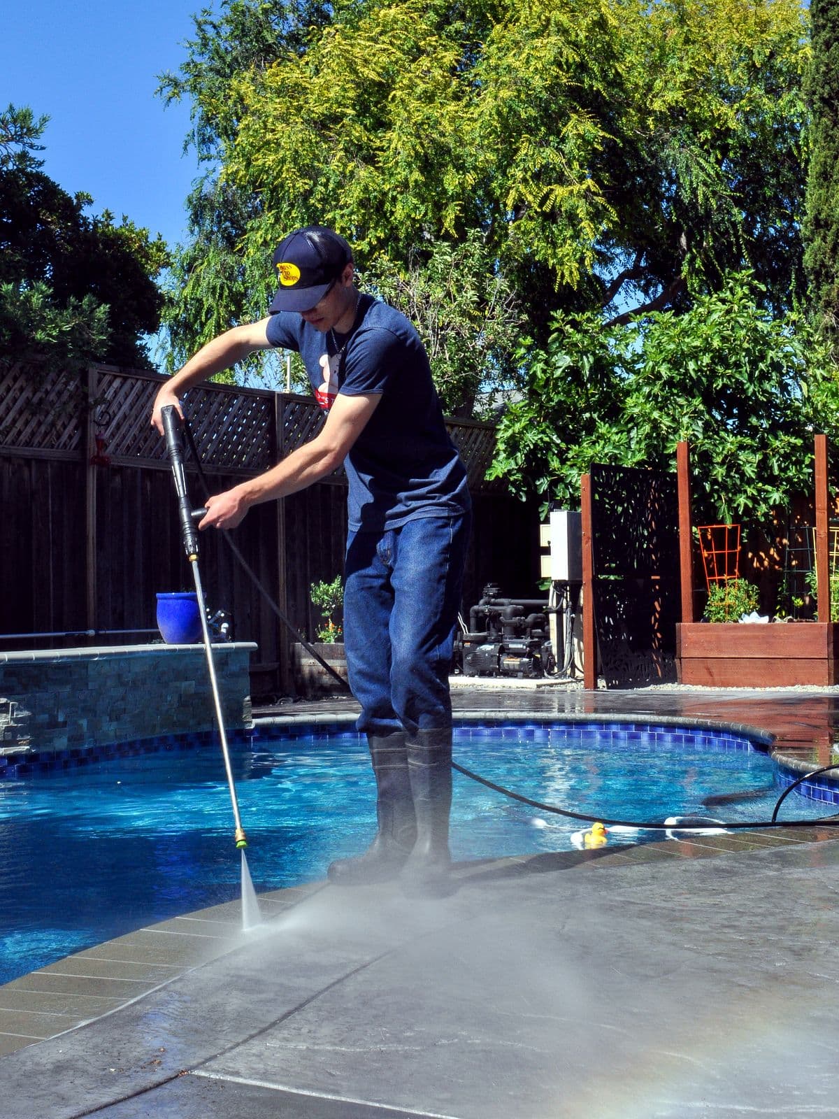 Bay Area Exterior Cleaning's owner pressure washing a backyard pool deck, with cleaning mist rising from the concrete.