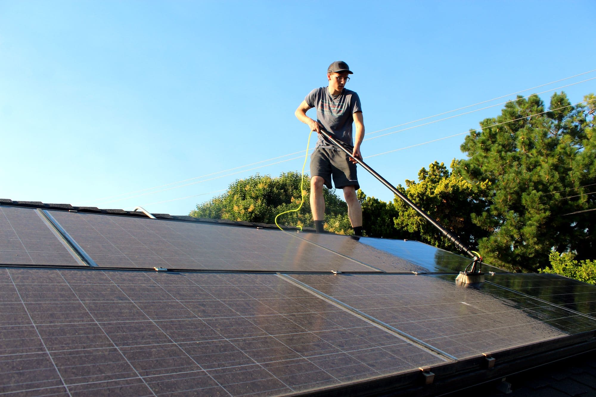 Bay Area Exterior Cleaning technician cleaning rooftop solar panels with a water-fed pole under a clear sky.